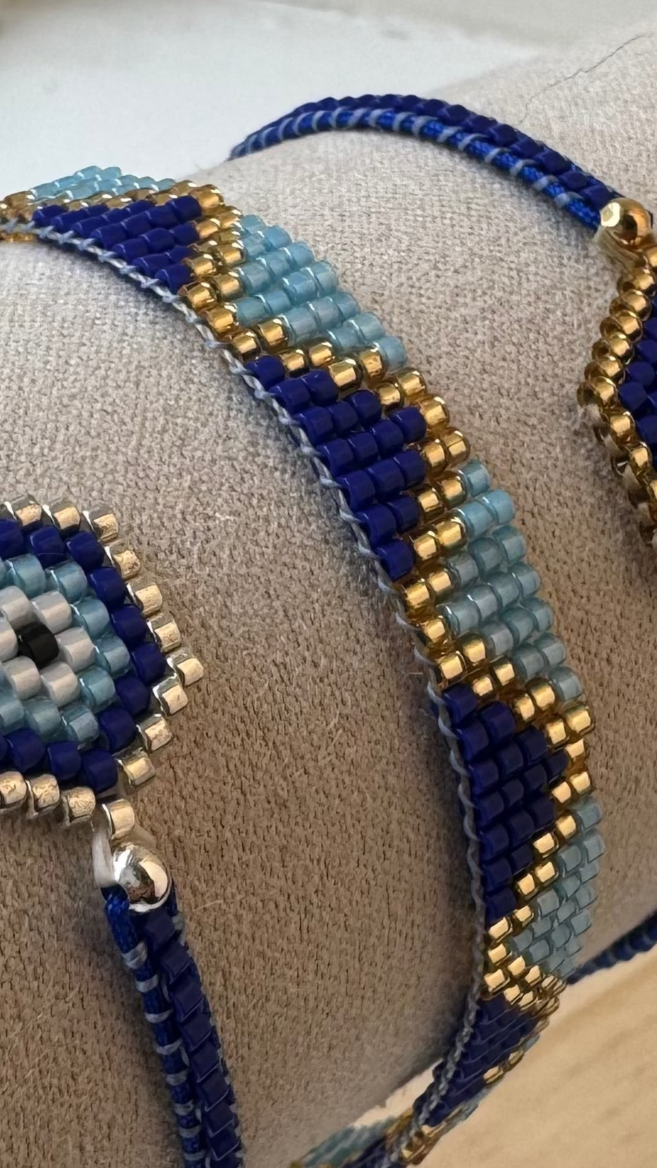 Two blue beaded bracelets on a wooden stand with a neutral background