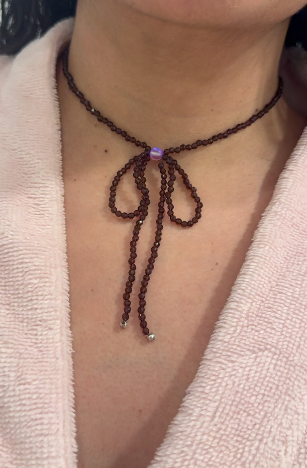 Necklace with a bow detail on a person wearing a light-colored garment.