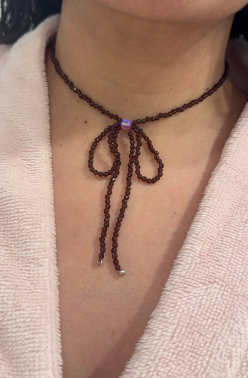 Necklace with a bow detail on a person wearing a light-colored garment.